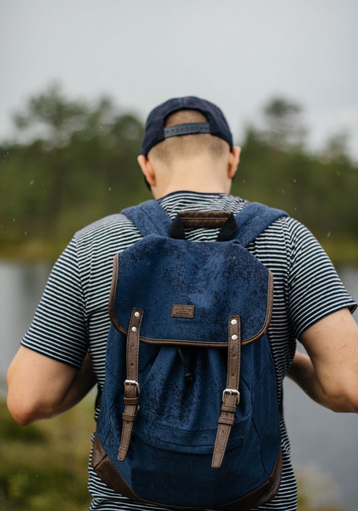 Person mit blauem Rucksack von hinten in der Natur